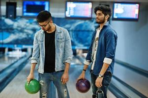 zwei südasiatische freunde im jeanshemd im bowlingclub, die bälle an den händen halten. foto