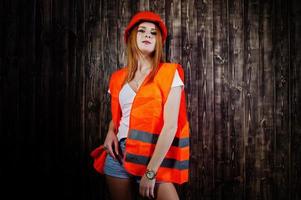 ingenieurin in orange schützt helm und gebäudejacke vor holzhintergrund. foto