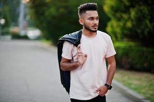 stilvoller indischer bartmann im rosa t-shirt mit schwarzer lederjacke auf der schulter. Indien-Modell zu Fuß in der Abendstadt. foto