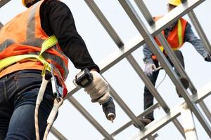 Bauarbeiter tragen Sicherheitsgurte, während sie auf einer Baustelle an der Dachkonstruktion des Gebäudes arbeiten. Dachdecker mit einer pneumatischen Nagelpistole. foto