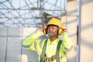 asiatische ingenieure in schutzhelmen und arbeiterschutzwesten mit schützenden kopfhörern auf baustellen. foto