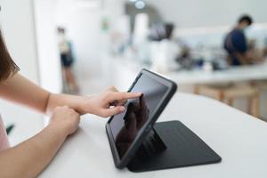 Frauenhand-Touchscreen auf digitalem Tablet während der Arbeit im Café. junges mädchen arbeitet auf dem tablet im internet, surft auf dem ipad, frau benutzt smartphone, hält tablet in der hand, sendet antwort. foto
