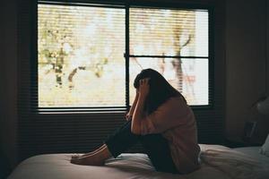 traurige asiatische frau, die unter depressionen leidet, schlaflosigkeit, wacht auf und sitzt allein auf dem bett im schlafzimmer. sexuelle Belästigung und Gewalt gegen Frauen, Gesundheitskonzept foto