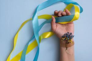 weibliche hand mit gelben und blauen bändern und blumen auf blauem hintergrund. liebe und bete zum ukrainischen konzept foto