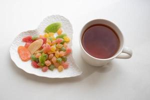 Teetasse aus Porzellan mit einem herzförmigen Teller mit Süßigkeiten auf weißem Hintergrund foto