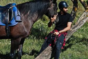 Arabischer Mann mit hohem Bart in schwarzem Helm mit arabischem Pferd. foto