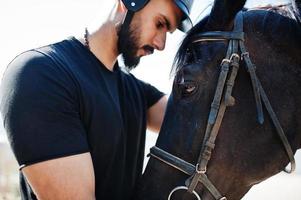 Arabischer Mann mit hohem Bart in schwarzem Helm mit arabischem Pferd. foto