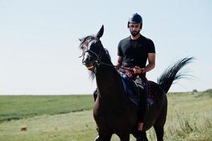 arabischer großer bartmann trägt schwarzen helm, reitet arabisches pferd. foto