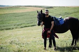 arabischer Mann mit hohem Bart in Schwarz mit arabischem Pferd. foto