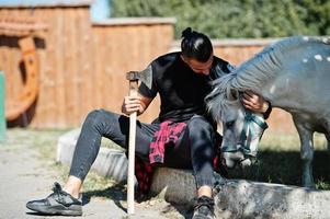 Arabischer Hipster-Bartmann-Holzfäller hält Axt gegen Ponypferd. foto