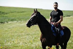 arabischer Mann mit hohem Bart trägt schwarzes arabisches Pferd. foto