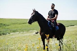 arabischer Mann mit hohem Bart trägt schwarzes arabisches Pferd. foto