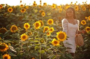 hübsche junge schwarze Frau tragen Sommerkleid Pose in einem Sonnenblumenfeld. foto