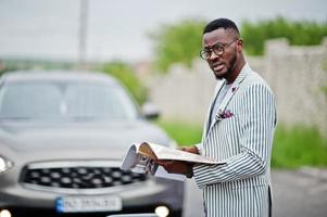 reicher und stilvoller afroamerikanischer mann in blazer und brille las zeitschrift gegen sein suv-auto. foto