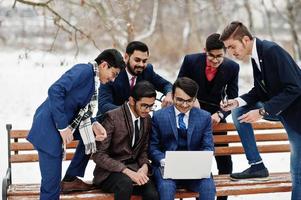 gruppe von sechs indischen geschäftsleuten in anzügen posierte im freien am wintertag in europa und schaute auf laptop. foto