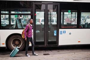 afroamerikanischer mann im karierten hemd, mit koffer und rucksack. Reisender des schwarzen Mannes gegen Bus. foto