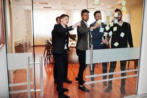 Geschäftsmann zeigt auf Glas mit bunten Papiernotizen. diverse gruppe männlicher mitarbeiter in formeller kleidung mit aufklebern. foto