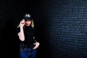 fbi-agentin in kappe und mit waffe im studio gegen dunkle backsteinmauer. foto