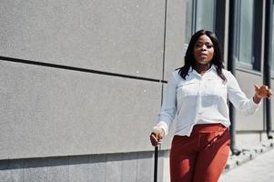 formell gekleidete afroamerikanische Geschäftsfrau in weißer Bluse und roter Hose mit Spazierstock zur Hand. erfolgreiche dunkelhäutige Geschäftsfrau. foto