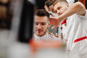 junger bärtiger mann, der vom friseur die haare schneiden lässt, während er im friseursalon auf dem stuhl sitzt. Barbier Seele. foto