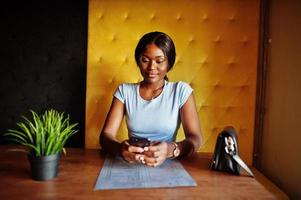 afrikanisch-amerikanisches Mädchen, das mit Handy im Café sitzt. schwarze Frau, die sich ausruht. foto