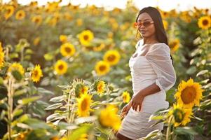 hübsche junge schwarze Frau tragen Sommerkleid Pose in einem Sonnenblumenfeld. foto