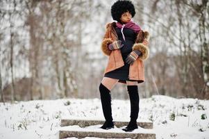 lockiges haar afroamerikanerin trägt schaffellmantel und handschuhe, die am wintertag gestellt werden. foto