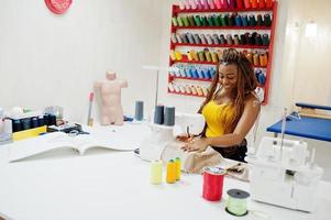 junge afrikanische schneiderin näht kleidung auf nähmaschine im schneiderbüro. schwarze Schneiderfrauen. foto