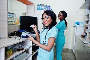 zwei afroamerikanische apotheker, die in der apotheke der krankenhausapotheke arbeiten. Afrikanisches Gesundheitswesen. arbeiten mit Zahlungsterminal und Kreditkarte. foto