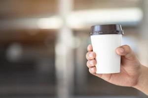 Menschen bemannen die Hand, die einen Pappbecher mit Kaffee zum Mitnehmen auf dem natürlichen Morgensonnenlicht hält, der im öffentlichen Park sitzt. Platz für Ihren Text oder Ihr Logo. foto