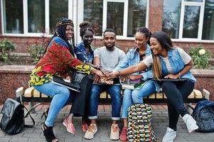 Gruppe von fünf afrikanischen College-Studenten, die gemeinsam Zeit auf dem Campus des Universitätshofs verbringen. schwarze afrofreunde, die an der bank mit schulsachen, laptops notizbüchern studieren. foto