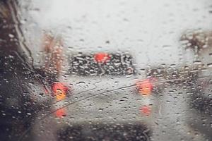 Abends rieseln Regentropfen auf die gläserne Windschutzscheibe. Straße bei starkem Regen. Bokeh-Rücklicht und Ampeln in der Stadt. Bitte fahren Sie vorsichtig mit dem Auto, rutschige Straße. Weicher Fokus. foto