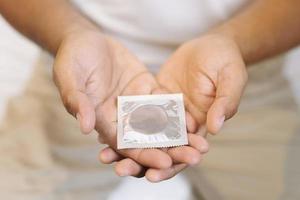 kondom gebrauchsfertig in männlicher hand, geben kondom safer sex konzept auf dem bett verhindern infektionen und kontrazeptiva kontrollieren die geburtenrate oder sichere prophylaxe. welt-aids-tag, lassen sie platz für text. foto