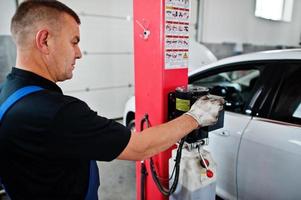 Thema Autoreparatur und -wartung. Mechaniker in Uniform, der im Autoservice arbeitet, Knopf drücken, um Auto anzuheben. foto