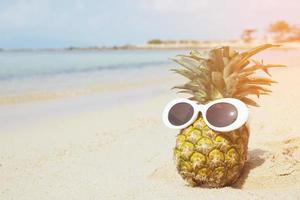 ananas mit stilvoller verspiegelter sonnenbrille auf dem sand gegen türkisfarbenes meer. tropische idee sommerferien am strandkonzept. Jahrgang filtern foto