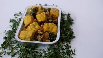 pflanzlicher tofu mit gelben gewürzen indonesisches essen serviert in einem aluminiumhalter mit weißem hintergrund mit ein paar grünen blättern drumherum foto