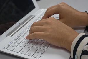 Frau sitzt am Schreibtisch und tippt auf der Tastatur eines weißen Laptops foto