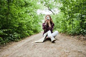 Porträt eines attraktiven blonden Mädchens mit einer Karte, das im Wald sitzt und Fotos macht.