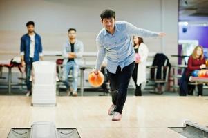 südasiatischer mann im jeanshemd, der an der kegelbahn steht und ball wirft. foto