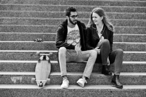 Cooles gemischtrassiges Paar, das mit Longboard auf der Treppe sitzt. foto