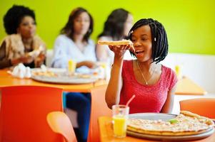 afrikanische frau mit pizza, die im restaurant gegen dunkelhäutige mädchen sitzt. foto