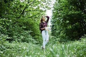 Porträt einer jungen schönen blonden Frau im Tartanhemd mit einer Karte im Wald. foto