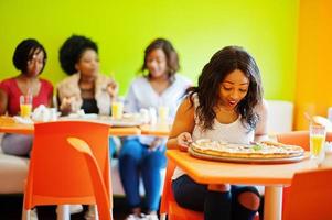 afrikanische frau mit pizza, die im restaurant gegen dunkelhäutige mädchen sitzt. überraschtes Gesicht. foto