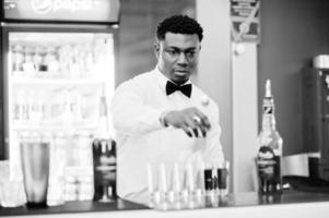 Afroamerikanischer Barkeeper an der Bar, der Cocktails auf Aufnahmen macht. Zubereitung von alkoholischen Getränken. foto