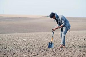 Südasiatischer agronomischer Bauer mit Schaufel, der schwarzen Boden inspiziert. landwirtschaftliches Produktionskonzept. foto