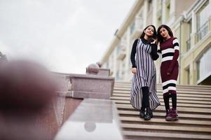 Porträt von zwei jungen schönen indischen oder südasiatischen Mädchen im Teenageralter im Kleid, das auf der Treppe in der Stadt posiert. foto