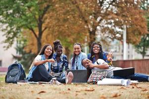 Gruppe von fünf afrikanischen College-Studenten, die gemeinsam Zeit auf dem Campus des Universitätshofs verbringen. schwarze Afro-Freunde sitzen auf Gras und lernen mit Laptops.