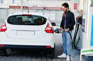 südasiatischer mann oder indischer mann, der sein weißes auto an der tankstelle betankt. foto