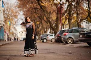 hübsches indisches mädchen im schwarzen saree-kleid posierte im freien auf der herbststraße. foto