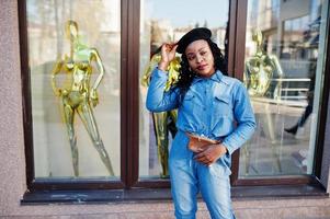 stilvolle modische afroamerikanische Frauen in Jeans und schwarzer Baskenmütze gegen modernes Gebäude mit drei goldenen Schaufensterpuppen. foto